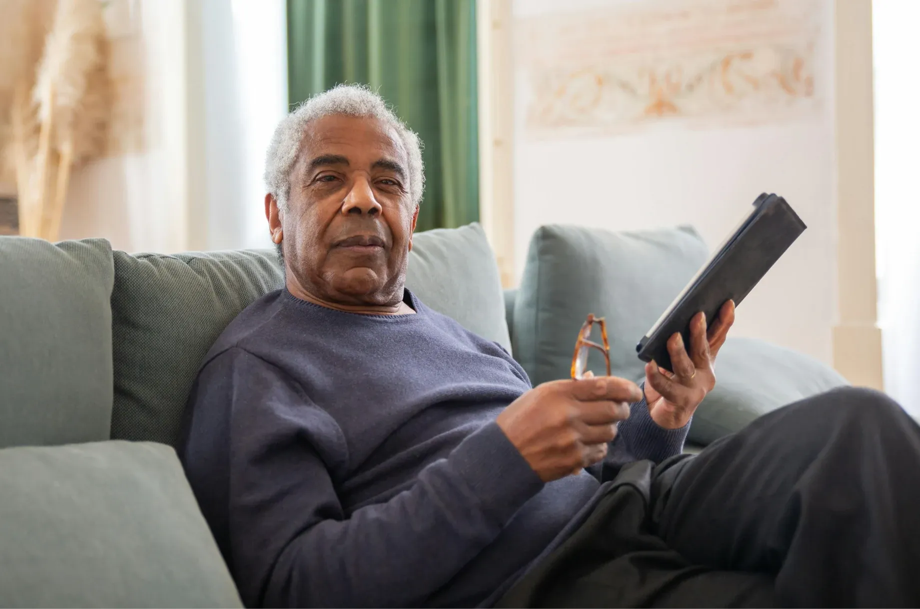 Retired man relaxing on a couch and reading on a tablet